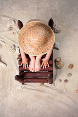 Little boy with straw hat, sitting on the ground, sea shells aro