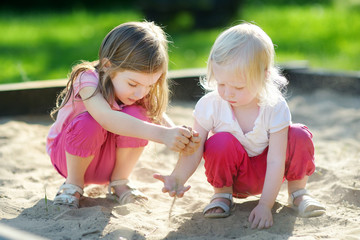 Wall Mural - Two little sisters playing in a sandbox