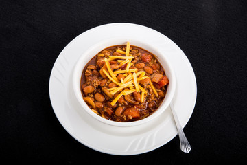 Wall Mural - White Bowl of Chili with Beans and Cheese on Black Background