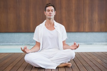 Handsome man in white meditating in lotus pose