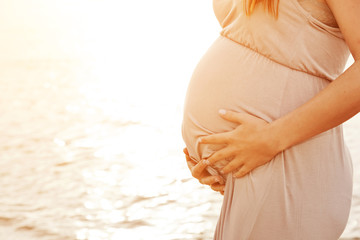 Pregnant woman on the beach touching her belly with love 