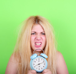 Portrait of sleepy young female in chaos holding clock against g