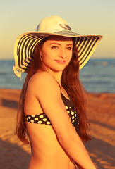 Wall Mural - Beautiful bikini woman in hat on sunset background looking