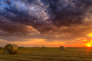 Wall Mural - Sunset over farm field with hay bales