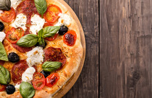 Rustic Pizza With Salami, Mozzarella, Olives And Basil On Wooden