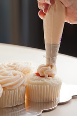 Gourmet strawberry filled cupcakes with white chocolate frosting - baker piping frosting