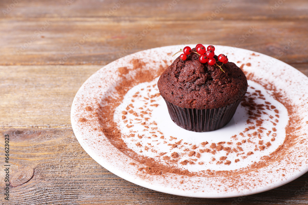 Chocolate muffin with red currant on plate on wooden background