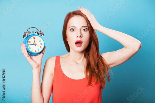 Fotografie, Obraz Surprised redhead women woth alarm clock on blue background.