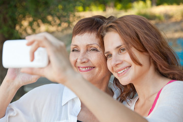 mother and adult daughter are doing selfie on phone