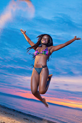 Beautiful black African American woman jumping on the beach at s