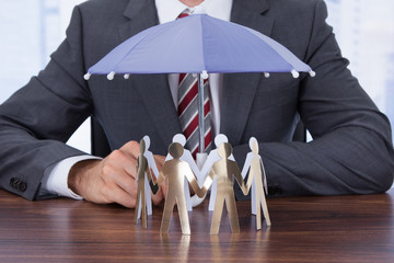 Wall Mural - Businessman Sheltering Paper People With Umbrella