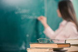 Fototapeta Tulipany - glasses and books with teacher writing at blackboard