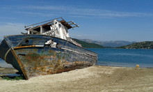 Shipwrecked Boat Beached On Sand With Sea And Mountains