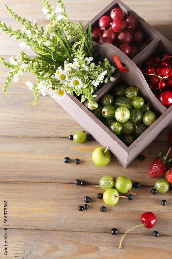 Fresh berries in wooden box and flowers on table, close up