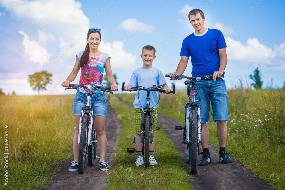 Happy family are riding bicycle in the field - obrazy, fototapety, plakaty 