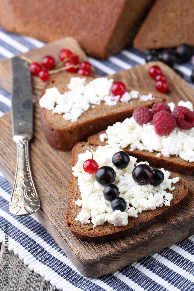 Bread with cottage cheese and berries on wooden board close-up