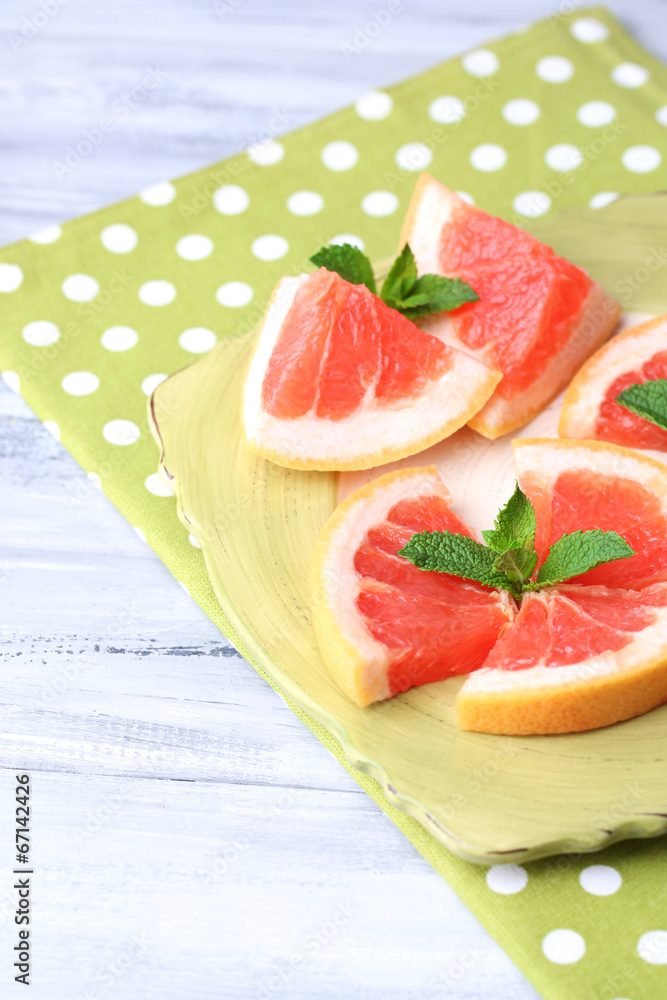 Ripe grapefruits on plate, on wooden table, on light background