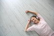 © goodluz - Blond girl relaxing on wooden flooring with headphones on
