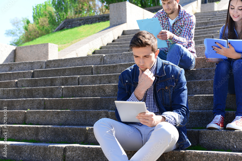 Happy students sitting on stairs in park