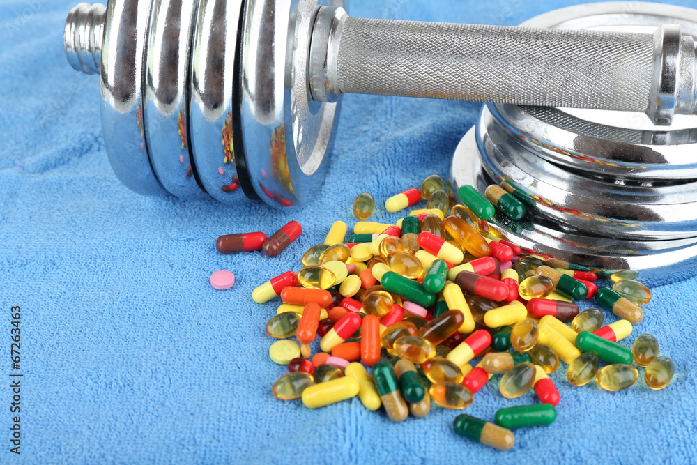 Dumbbell and colorful pills, tablets, on color background