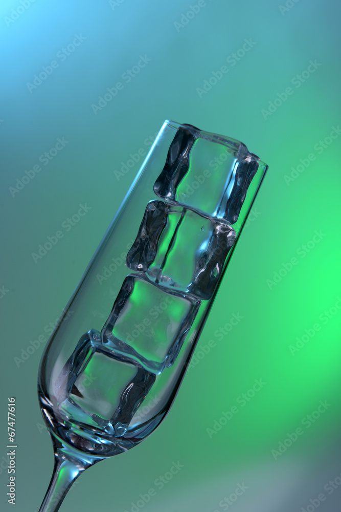 Glass with ice cubes on color background