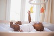 Adorable afro-american baby boy lying in his crib playing with mobile