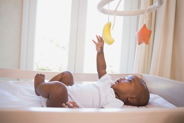 adorable afro-american baby boy lying in his crib playing with mobile