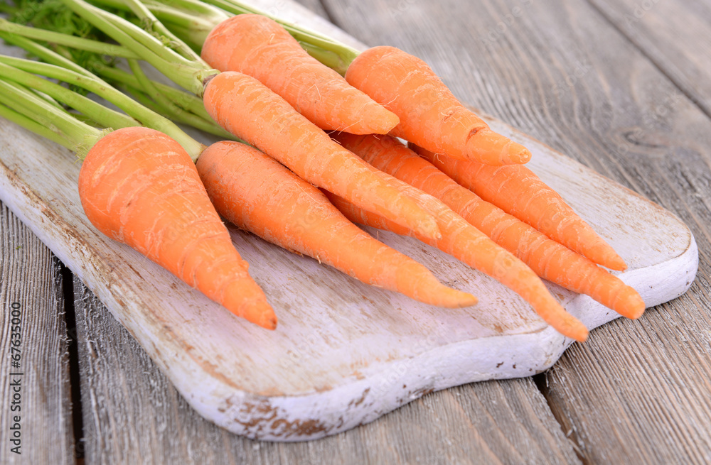 Fresh carrot on cutting board on wooden background