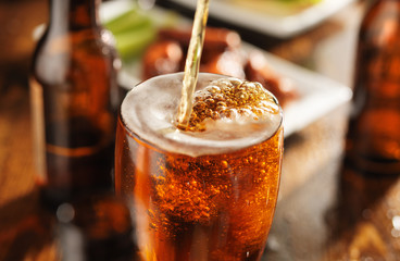 pouring beer into glass with bbq chicken wings in background