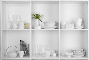 Different white clean dishes on wooden shelves