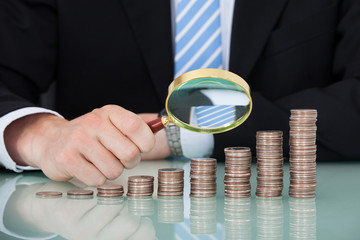 Businessman Examining Coins Stacked As Bar Graph