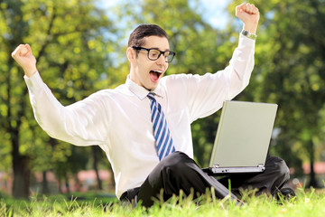 Poster - Young man cheering and watching TV on a laptop in park