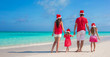 © travnikovstudio - Back view young family of four in Santa Hat on tropical beach