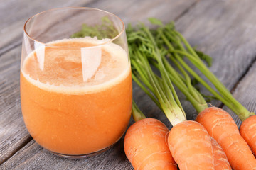 Wall Mural - Glass of carrot juice and fresh carrots on wooden background