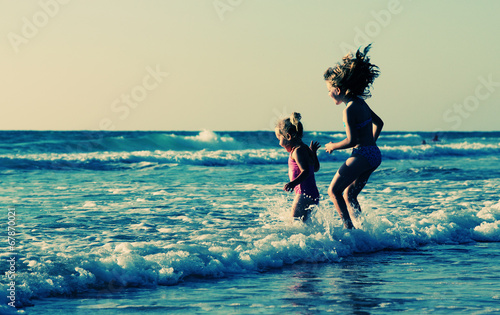 Fotoboard na płycie Dwa szczęśliwe dzieci bawiące się na plaży o zachodzie słońca