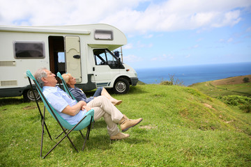 Wall Mural - Senior couple relaxing in camping folding chairs, sea landscape