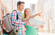 smiling couple with map and backpack in city