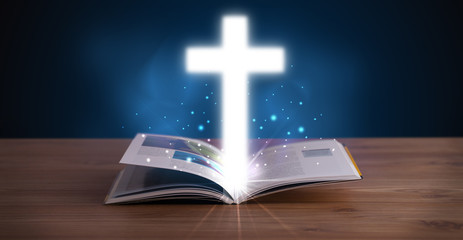 Open holy bible with glowing cross in the middle