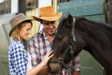 Cowboy And Cowgirl Comforting A Horse In Stable