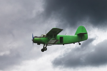 Wall Mural - small green airplane flying in dark grey sky