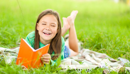 Wall Mural - Little girl is reading a book outdoors