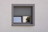 Fototapeta Kwiaty - Dunkles Kunststofffenster mit Rollladen in grauer Fassade