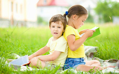 Wall Mural - Little girl and boy are reading book outdoors