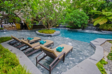 Poolside relax chairs in garden style swimming pool