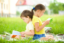 Little Girl And Boy Are Reading Book Outdoors