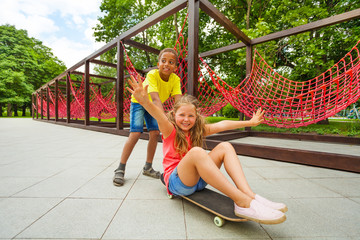 Boy pushing girl sitting on skateboard and roll