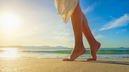 Canvas Print - Young woman in white dress walking alone on beach in sunrise