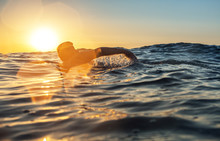 Young Man Swiming In The Sea Over Yellow Sunrise