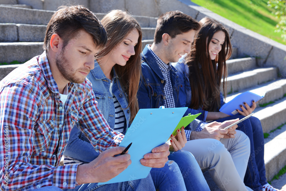 Happy students sitting on stairs in park