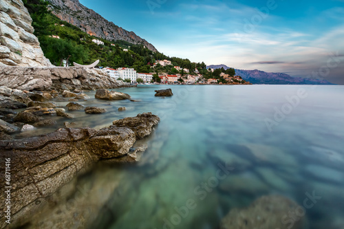 Plakat na papierze fotorealistycznym Skalista plaża i mała wioska w pobliżu omis o zmierzchu, Chorwacja
